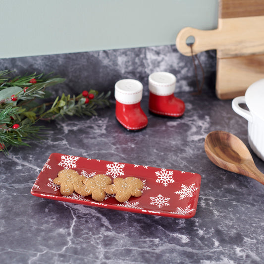 Red plate with snowflake design holding cookies, next to red boot-shaped containers on a gray surface.