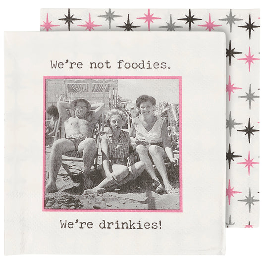 Cocktail napkin with vintage photo of people at a beach and text 'We're not foodies. We're drinkies!' on a patterned background.