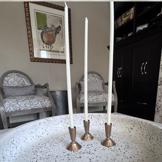 Three white taper candles in bronze candle holders