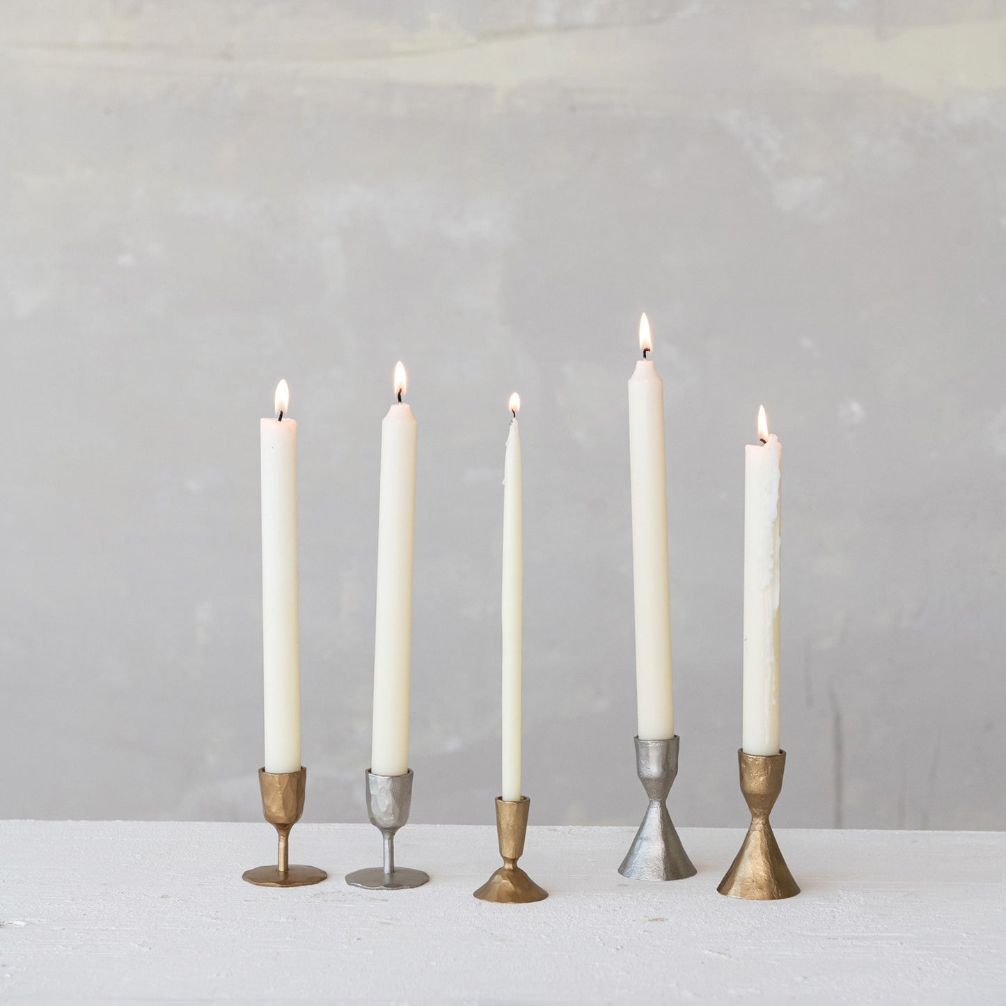 Five candles in various candle holders on a white surface with a gray background