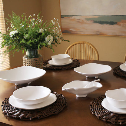 Dining table set with white melamine dishes and a vase of flowers on a wooden table.