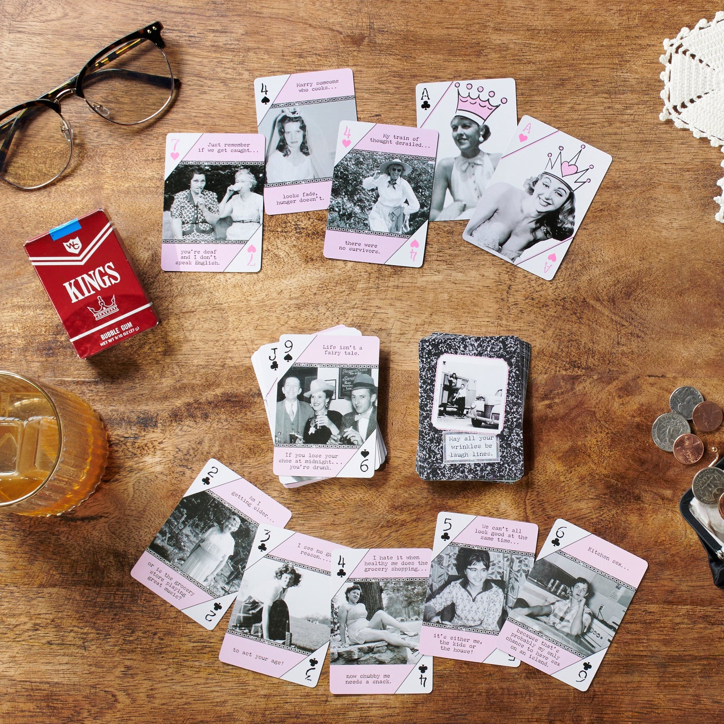 1960' themed paying cards with vintage images on a wooden table with a Kings cigarettes box.