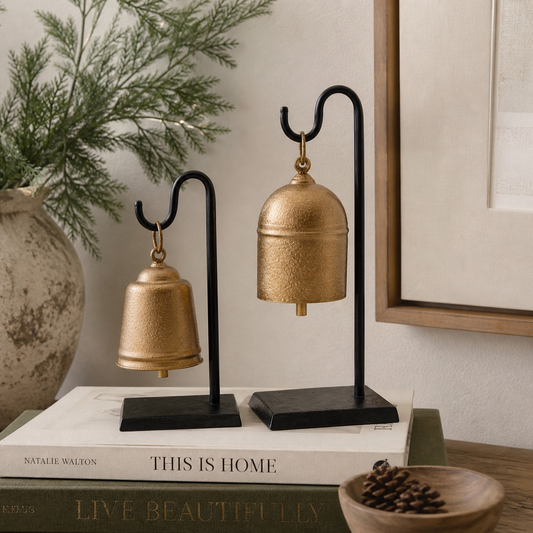 2 vintage inspired antique gold bells on a black stand surrounded by  holiday decor 