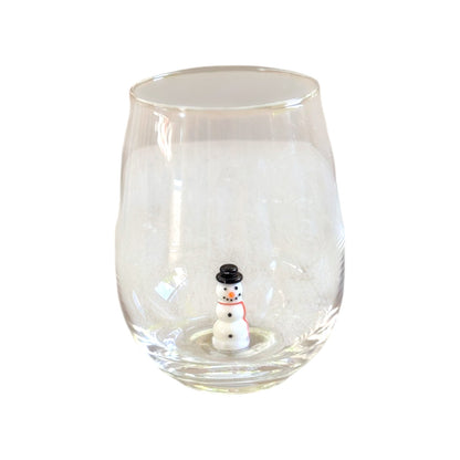 A clear stemless wine glass with a small snowman figurine sitting inside the base, set against a plain white background.