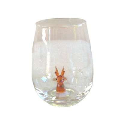A clear stemless wine glass featuring a small orange and white deer figurine embedded in the base, set against a plain white background.