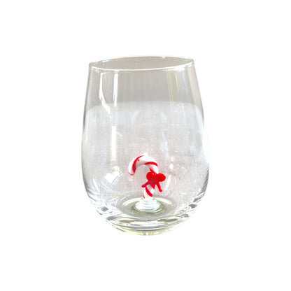 A clear stemless wine glass featuring a small red and white candy cane figure molded into the base, set against a plain white background.