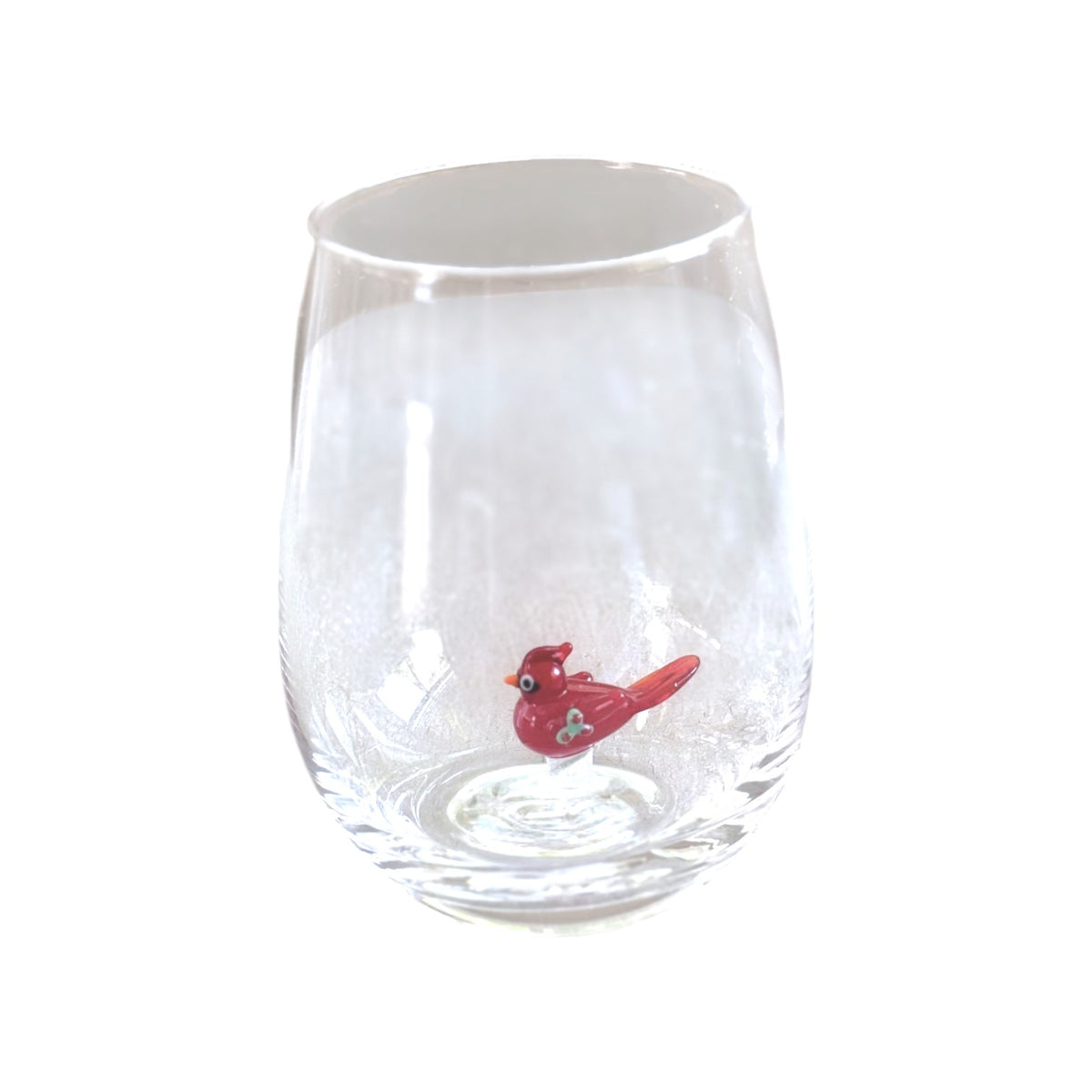 A clear stemless wine glass featuring a small red bird figurine sitting inside the base, set against a plain white background.