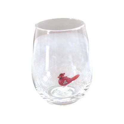 A clear stemless wine glass featuring a small red bird figurine sitting inside the base, set against a plain white background.