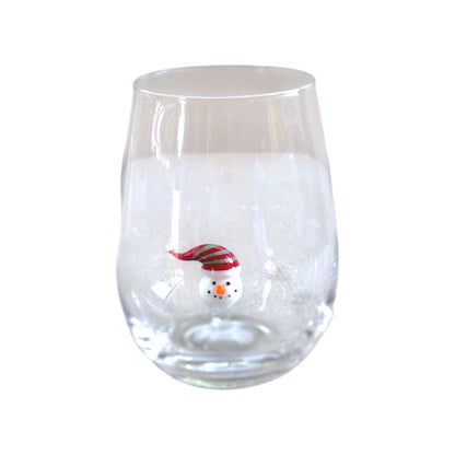 A clear stemless wine glass featuring a small snowman decoration wearing a red and green striped Santa hat near the bottom center.