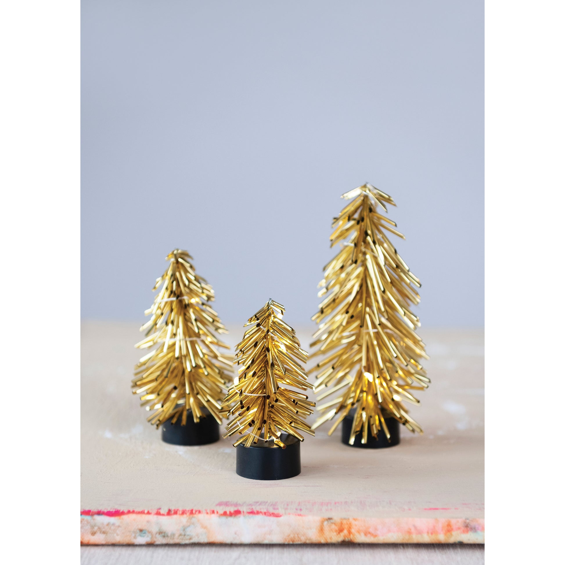 Three gold metallic Christmas trees on a light background, with LED lighting