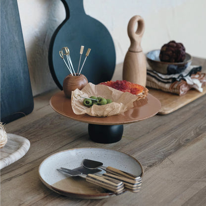 Table setting with a cake stand, plates, and cutlery on a wooden surface.