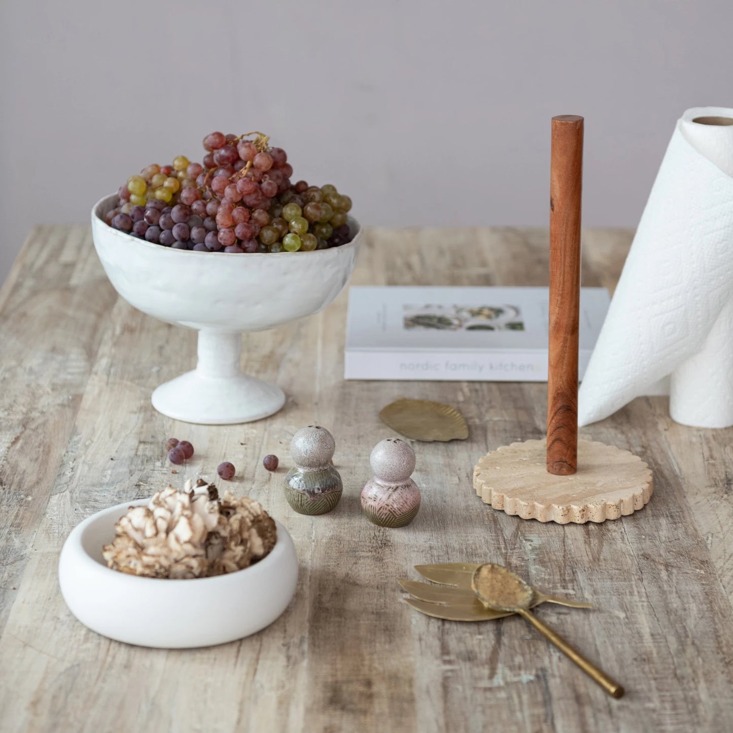 White ceramic footed bowl with grapes on a wooden table with decorative items.