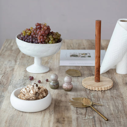 White ceramic footed bowl with grapes on a wooden table with decorative items.