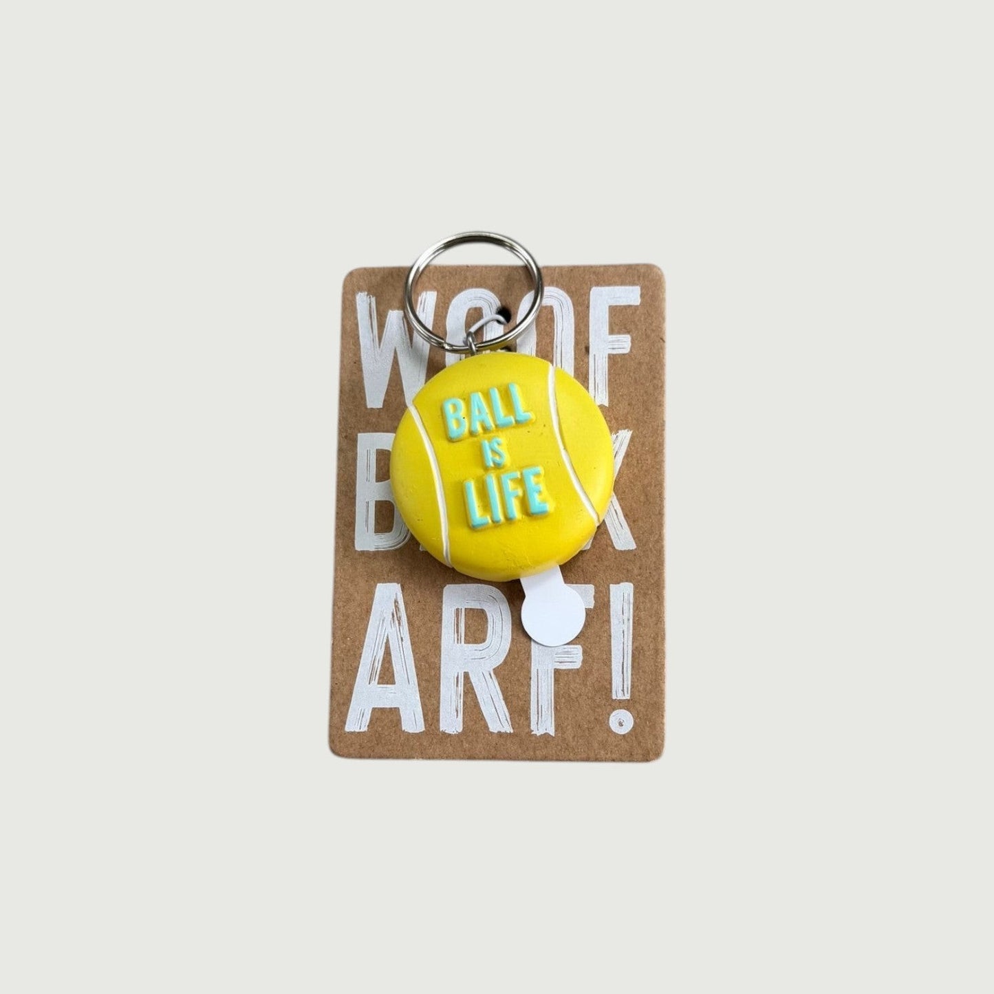 CJ Gift Goddess yellow tennis ball keychain with "Ball is Life" text, attached to a cardboard backing with "Woof" and "Arf!" text.