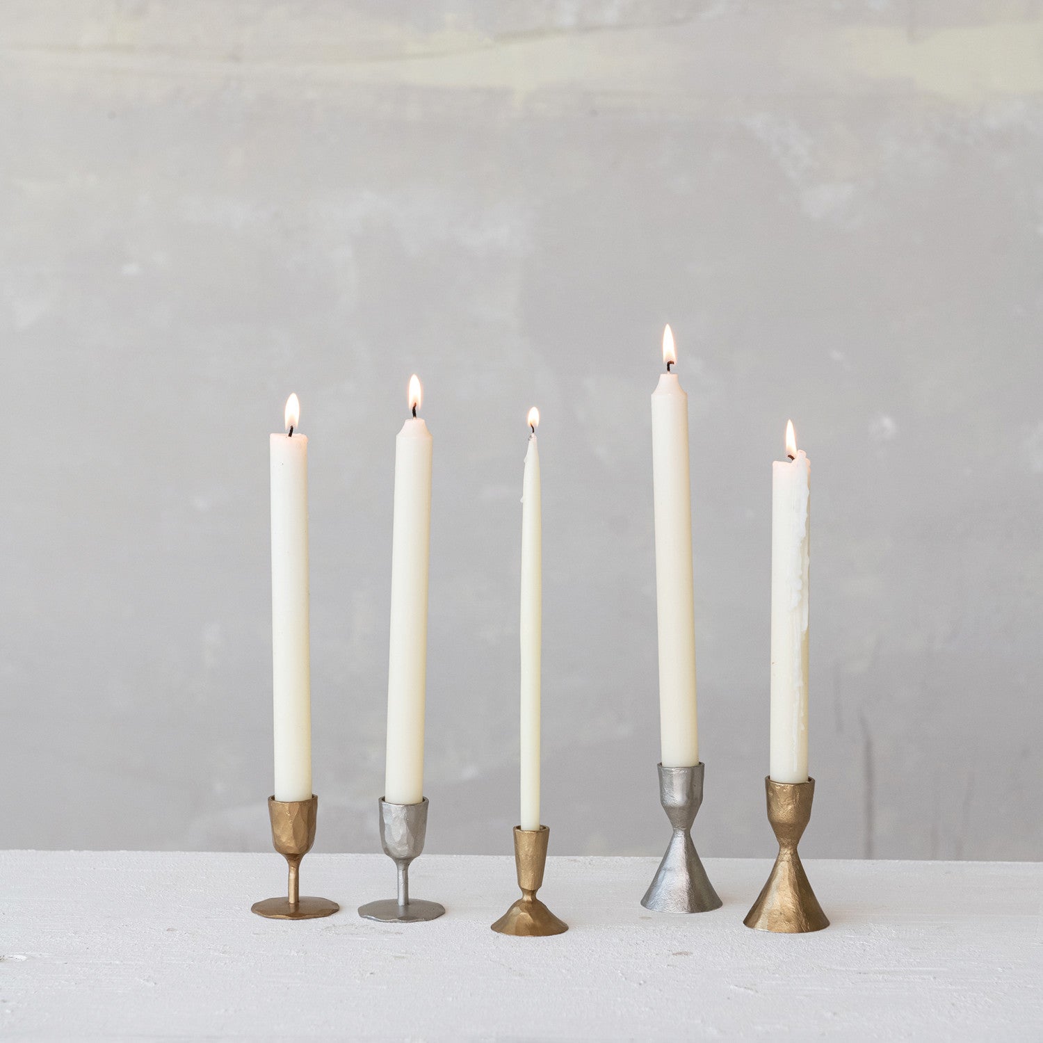 Five candles in various candle holders on a white surface with a gray background