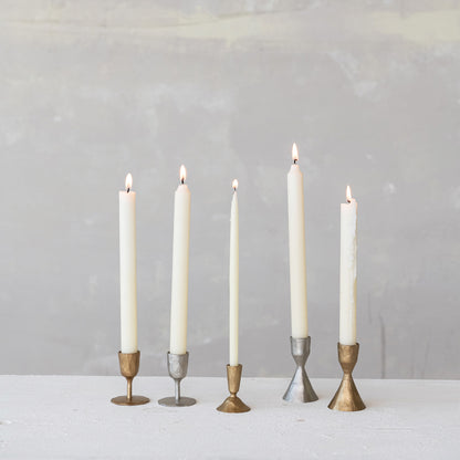 Five candles in various candle holders on a white surface with a gray background