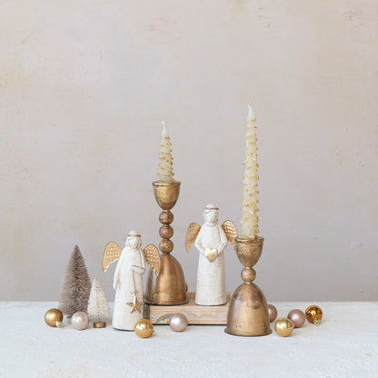 Decorative setup with antique gold candlesticks, angel figurines, and small trees on a white surface.