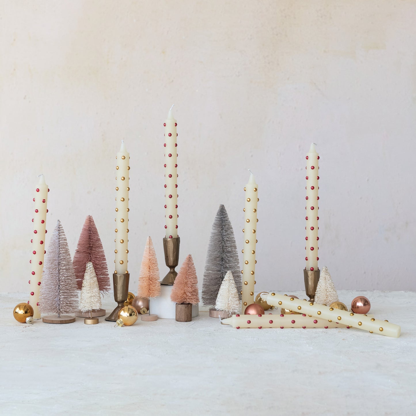 Decorative setup with candles, small trees, and ornaments on a white surface.