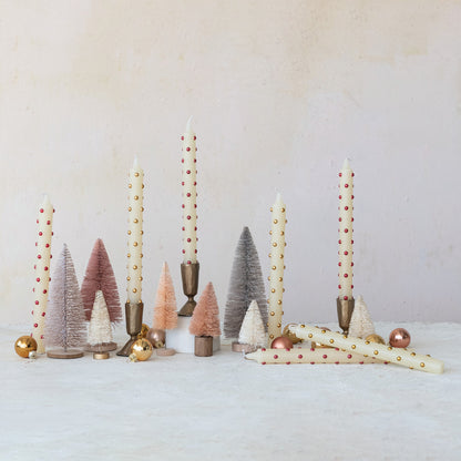 Decorative setup with candles, small trees, and ornaments on a white surface.